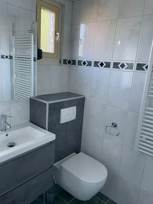 Hangtoilet tegen een antraciet voorzetwand met drukplaat, naast een grijs lavabomeubel
