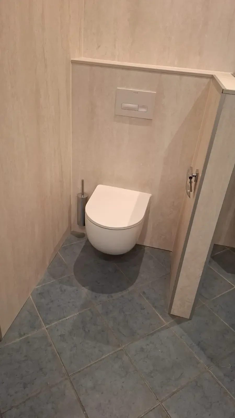 Hangtoilet tegen een voorzetwand met beige steenlook panelen en blauwgrijze vloertegels