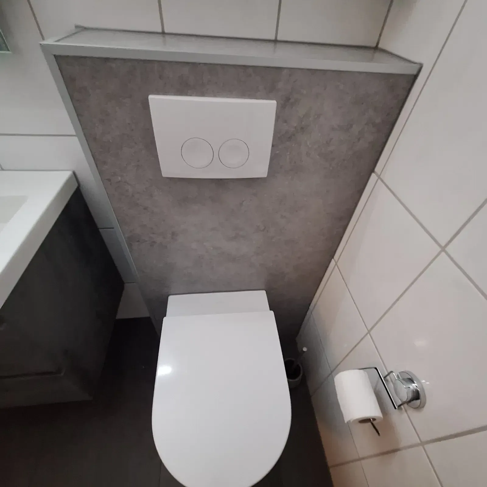 Hangtoilet met een grijze steenlook voorzetwand, witte drukplaat en toiletrolhouder