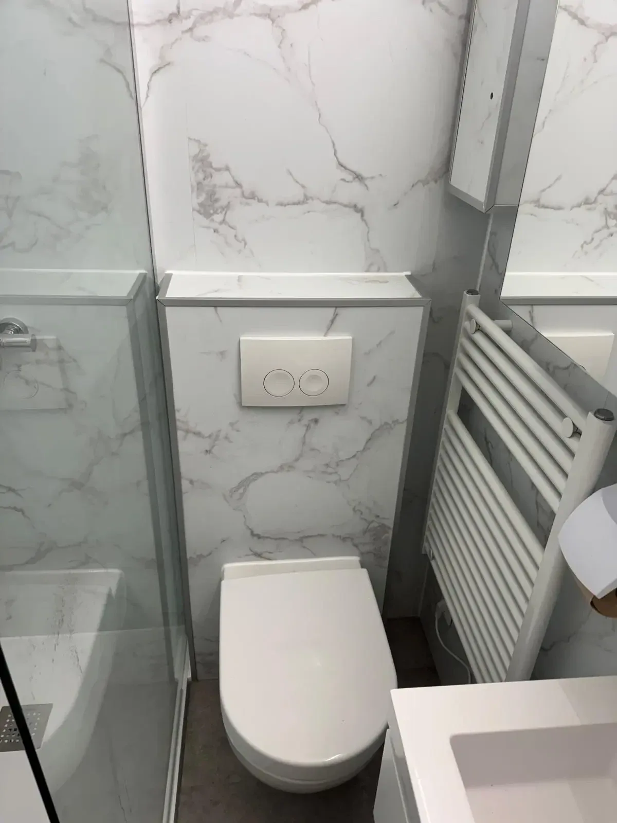 Wit hangtoilet op een voorzetwand met witte marmerlook panelen en een witte handdoekradiator