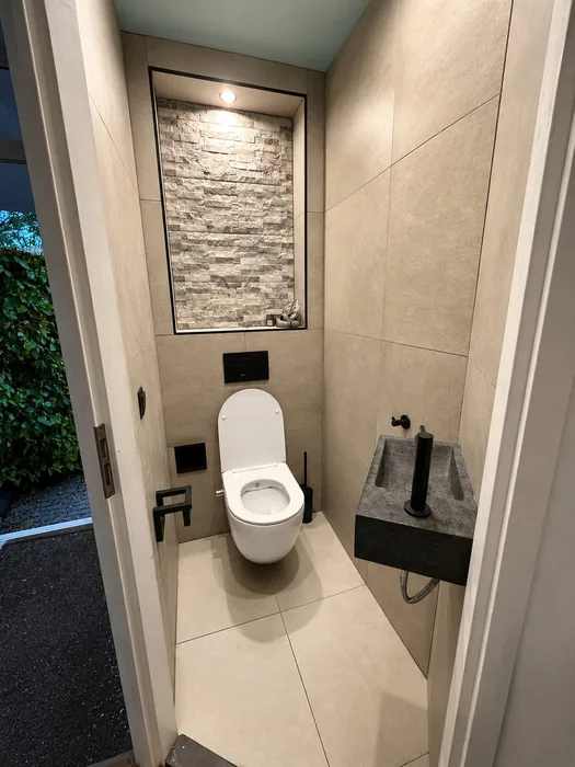 Wc met hangtoilet, natuurstenen handwasbakje en een verlichte nis met steenstrips