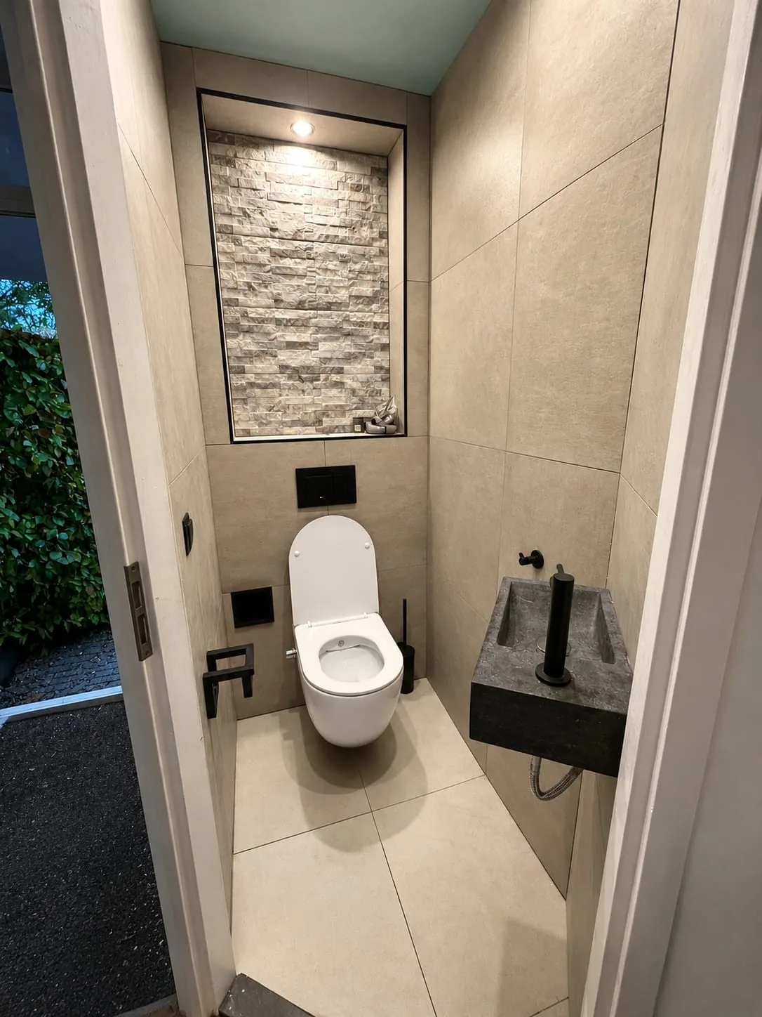 Wc met hangtoilet, natuurstenen handwasbakje en een verlichte nis met steenstrips
