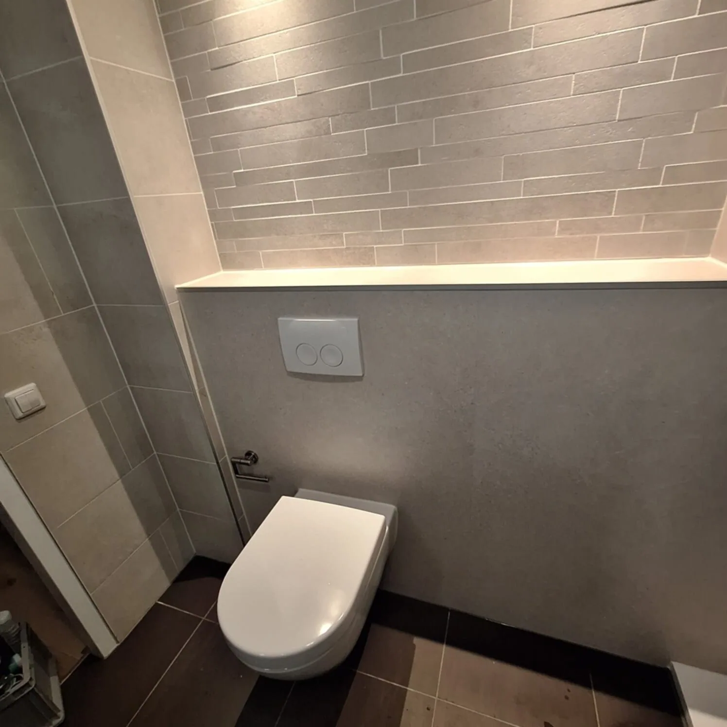 Hangtoilet tegen een grijze voorzetwand met verlichte nis en een wand van smalle stroken erboven