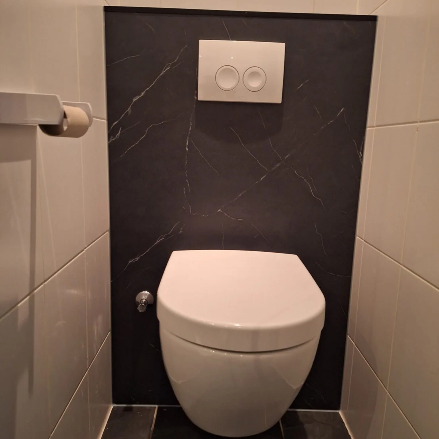 Hangtoilet voor een zwart marmerlook paneel met witte drukplaat, witte wandtegels opzij