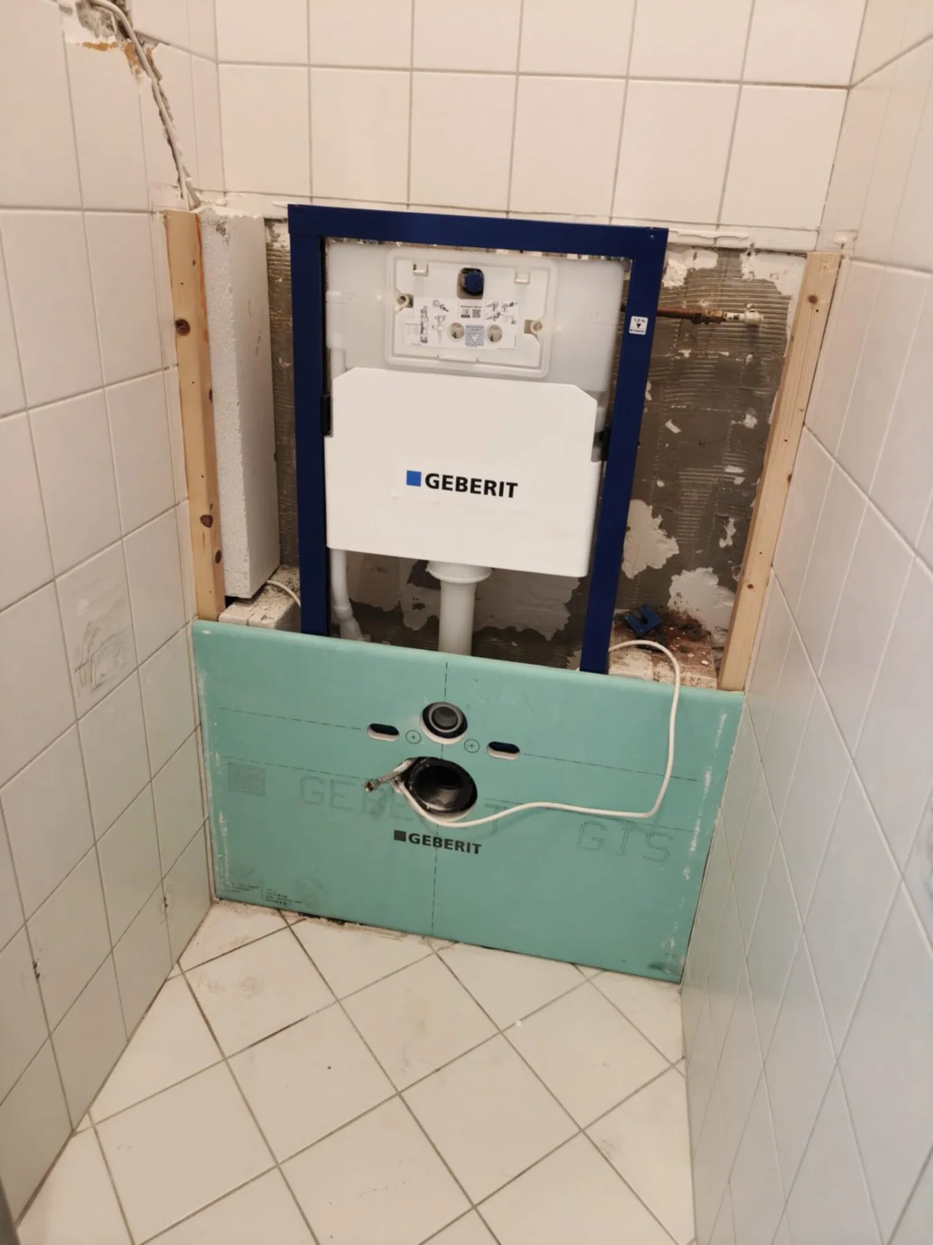 Inbouwframe voor een hangtoilet met groene voorzetwandplaat tussen witte wandtegels