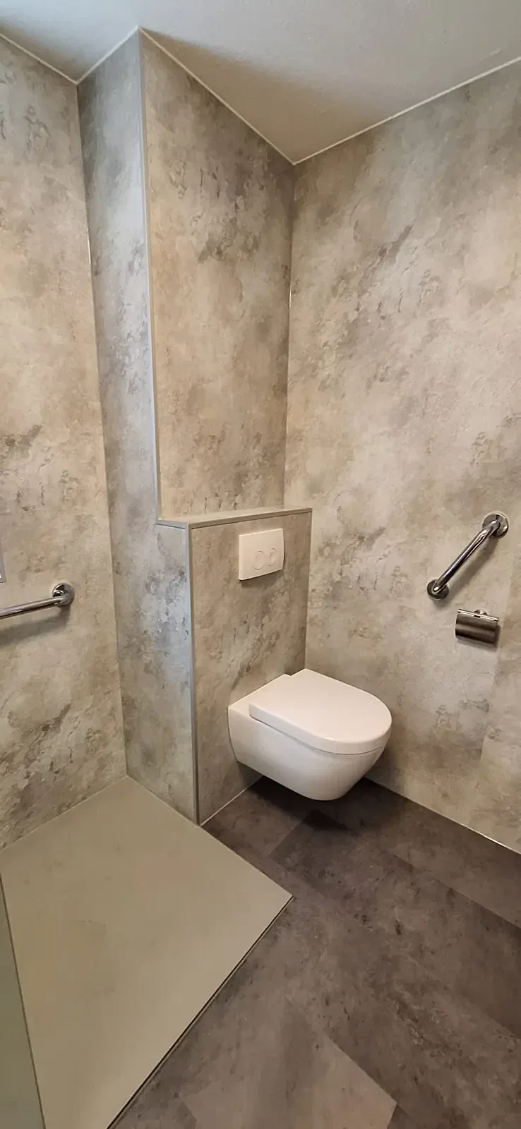 Hangtoilet op een voorzetwand met beige marmerlook panelen en steunbeugels aan beide kanten