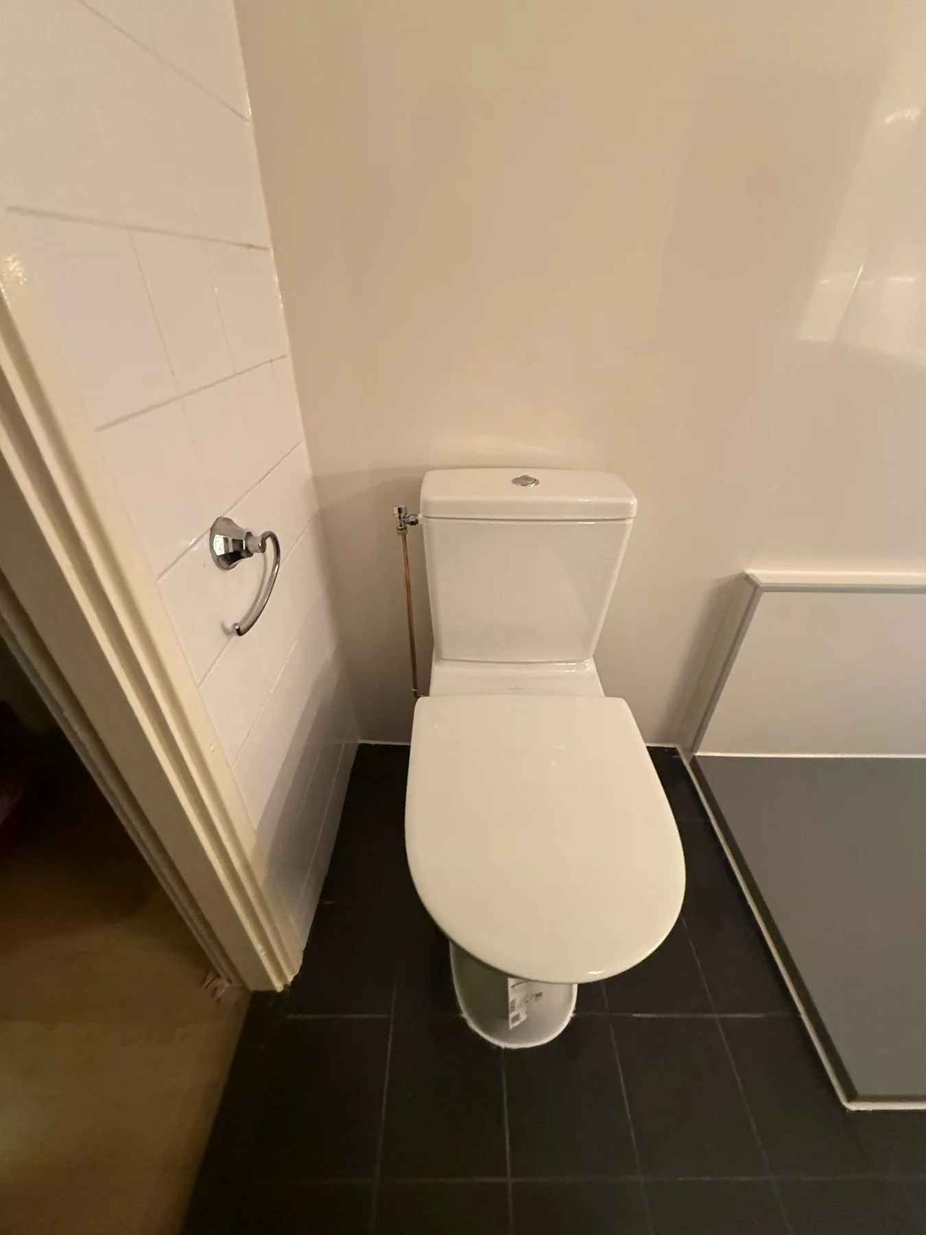 Wit staand toilet op donkere vloertegels naast een witte wand
