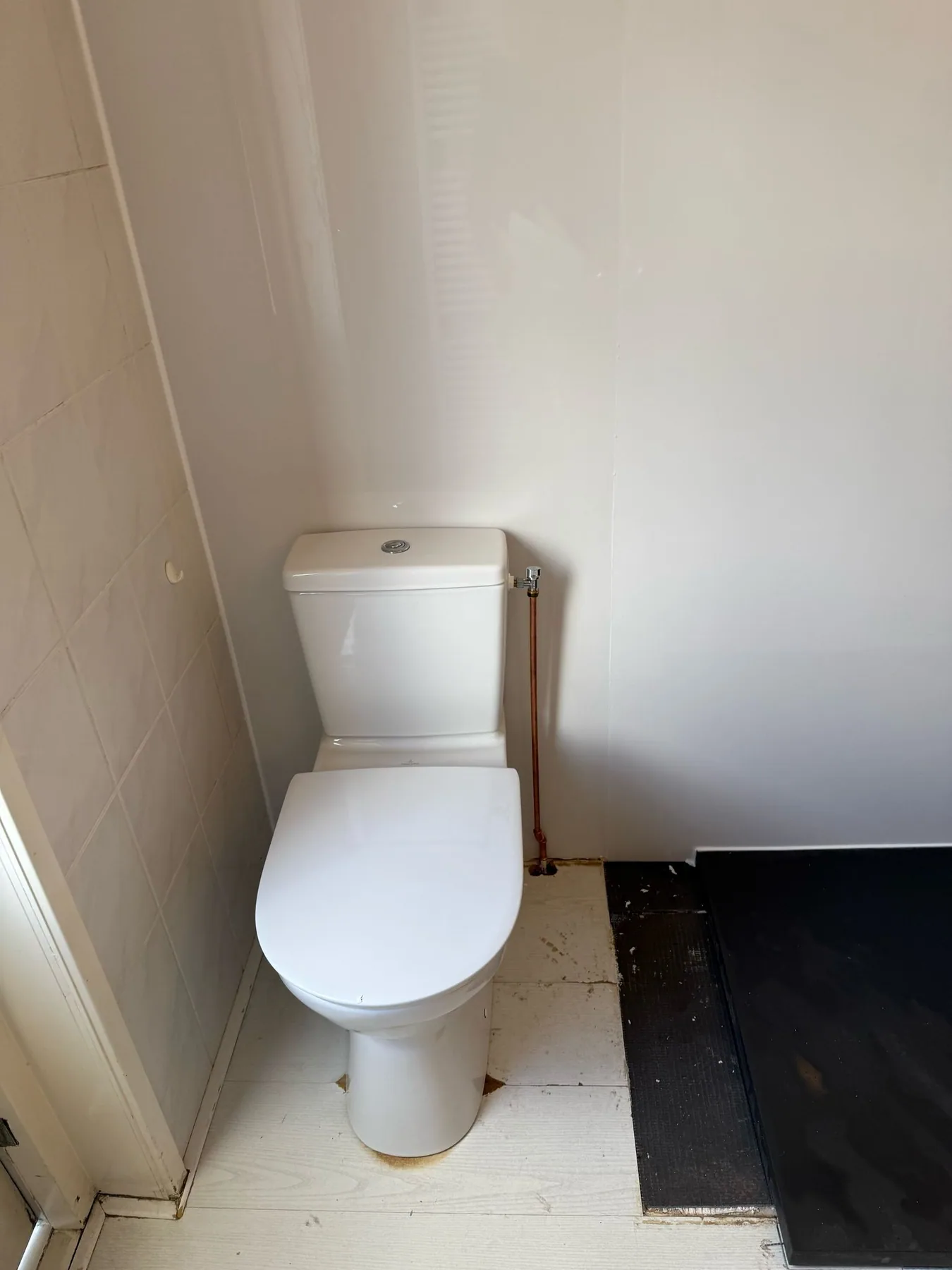 Nieuw staand toilet tegen witte wandpanelen, de vloer nog deels afgedekt