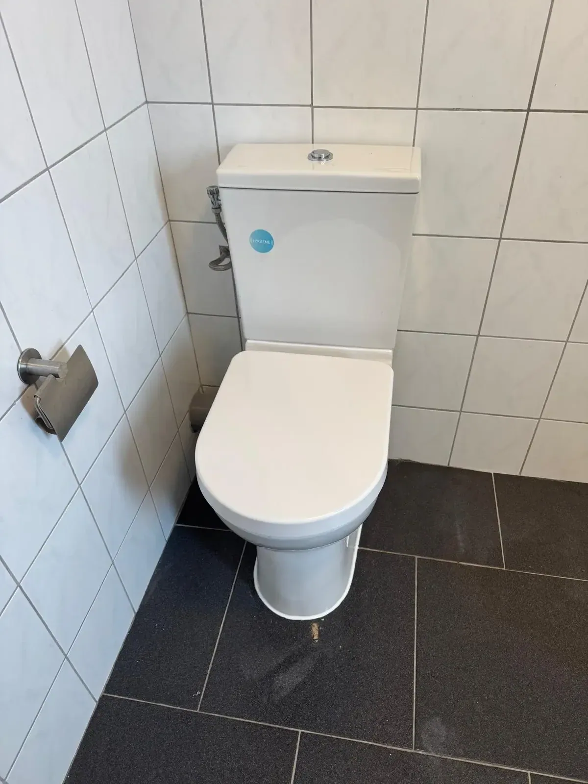 Nieuw wit staand toilet met duoblok tegen witte wandtegels op een donkere vloer