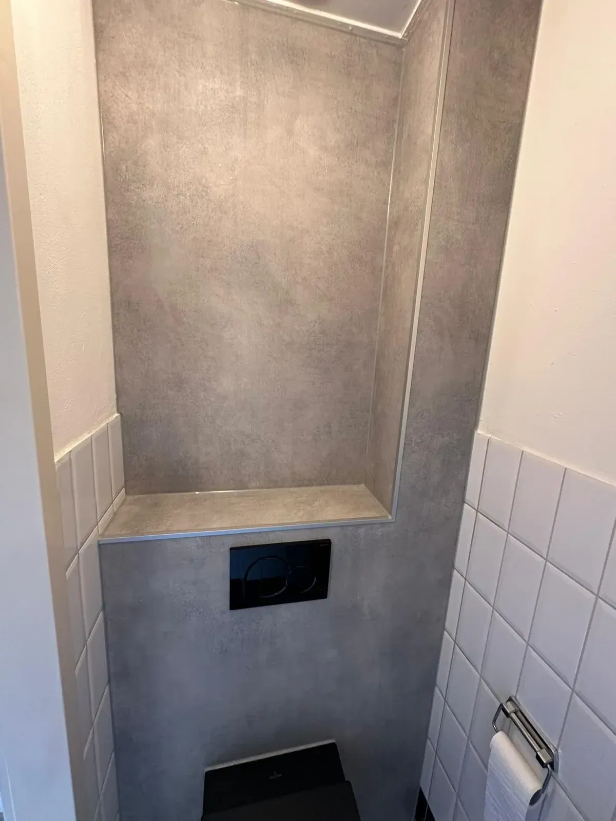 Wc met grijze panelen boven een voorzetwand met zwarte drukplaat en witte tegels opzij