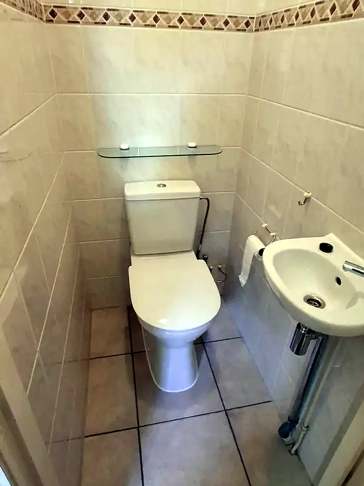 Vóór: smalle wc met lichte tegels, sierrand, staand toilet en handwasbakje