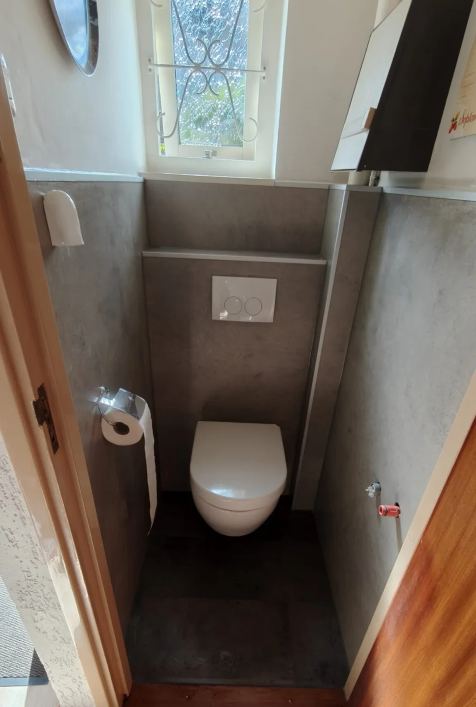 Na: dezelfde wc met hangtoilet, voorzetwand met witte drukplaat en grijze betonlook wandpanelen