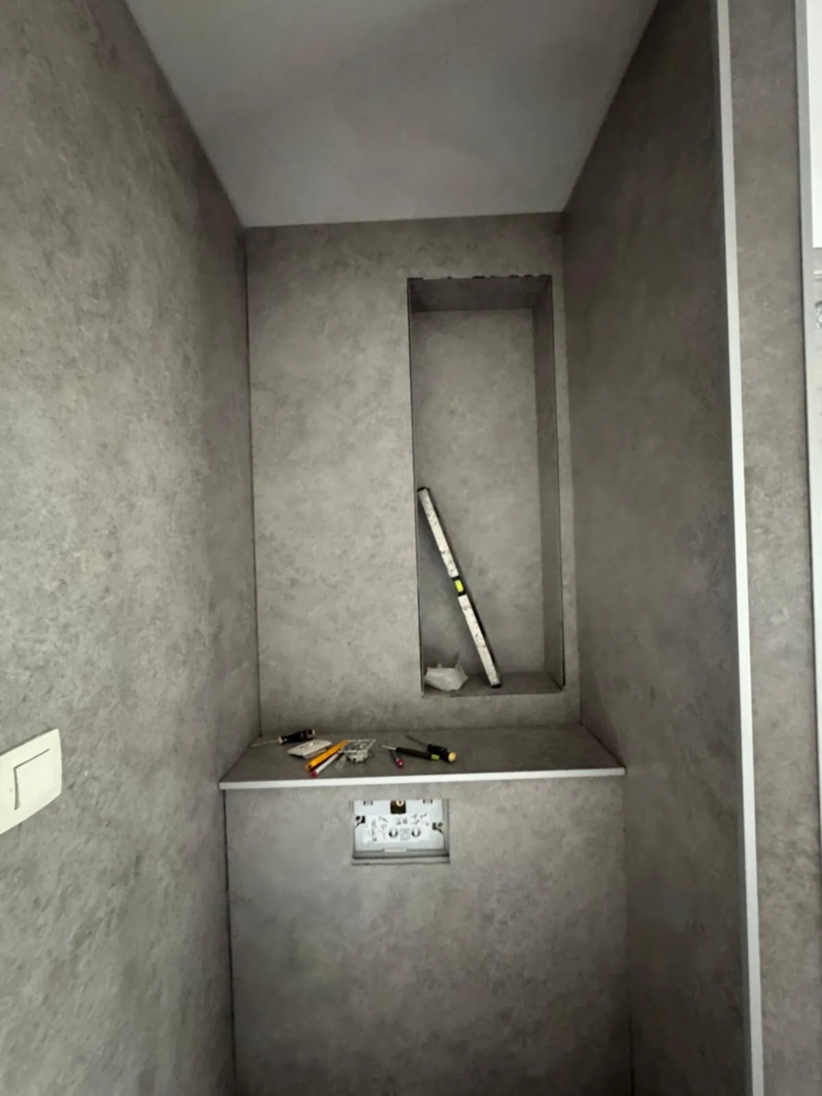 Voorzetwand met nis voor een hangtoilet, al bekleed met grijze steenlook panelen