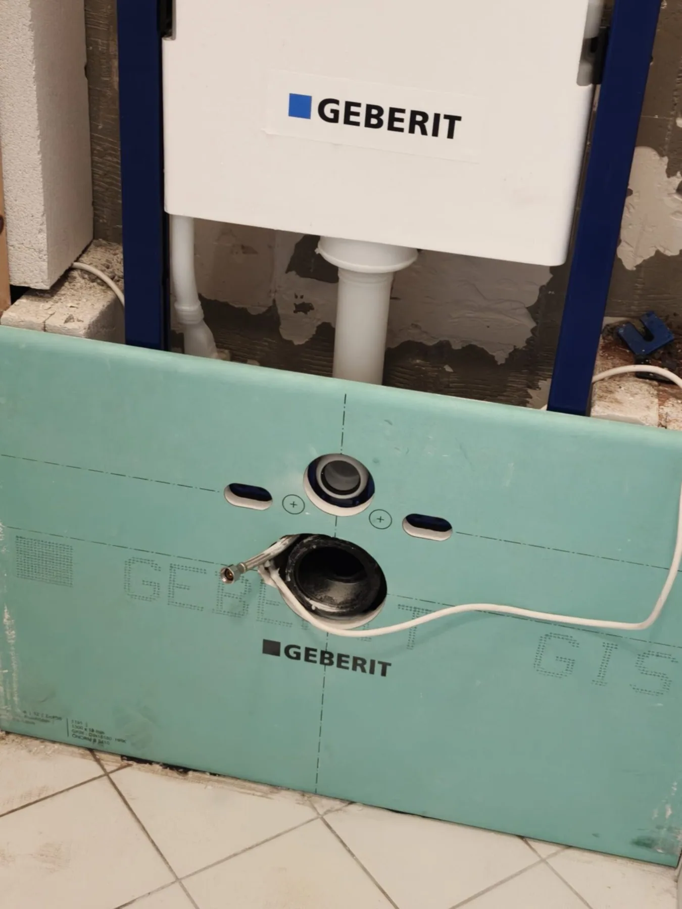 Close-up van het inbouwreservoir met groene voorzetwandplaat en de aansluitingen voor het hangtoilet