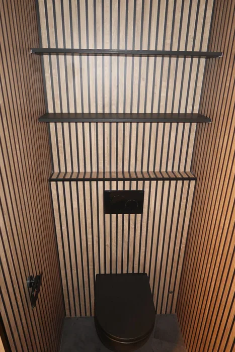Wc met houten lamellen op de wanden, een zwart hangtoilet, zwarte drukplaat en zwarte wandplanken