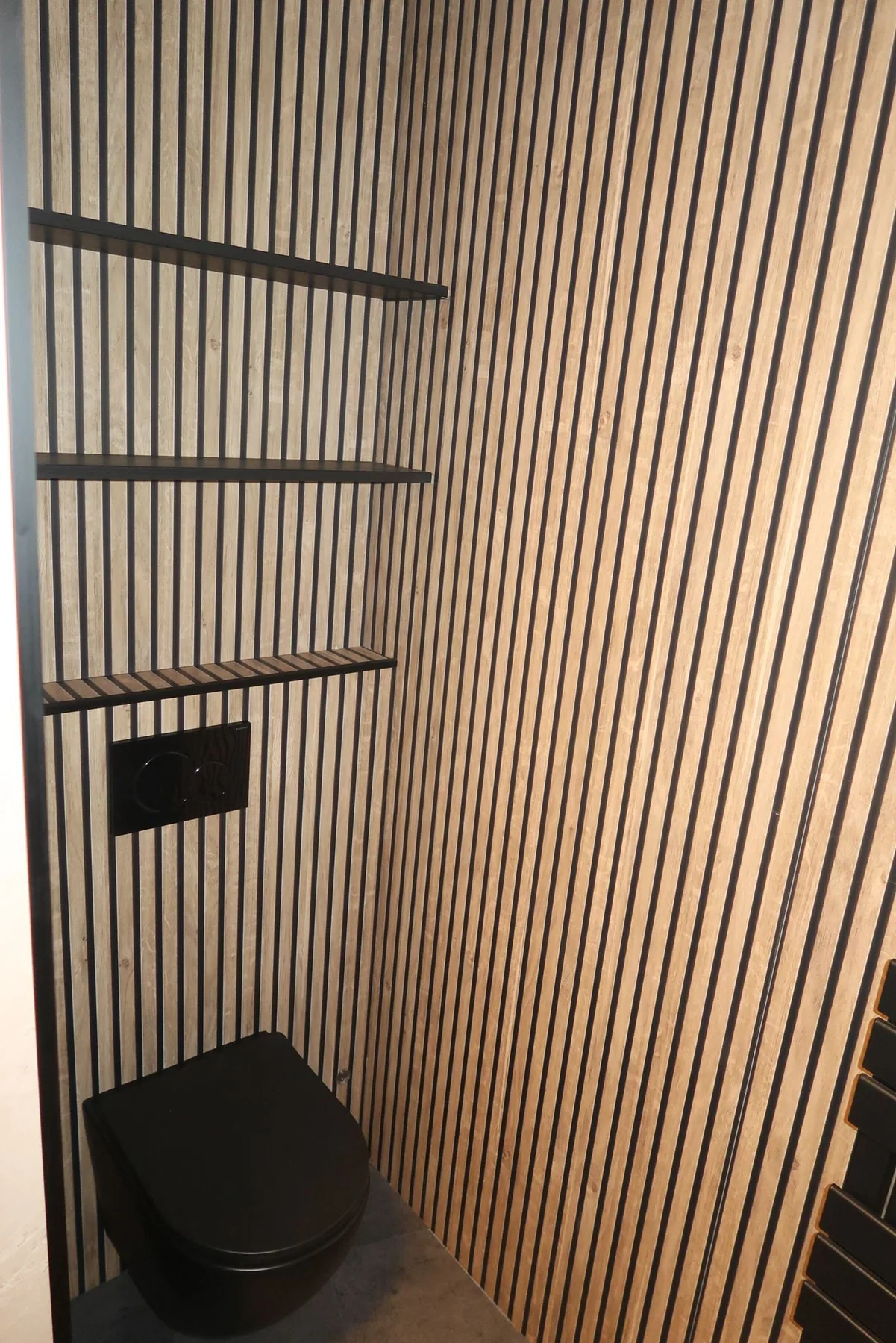 Dezelfde wc met lamellenwand en zwart hangtoilet, gezien vanuit de deuropening