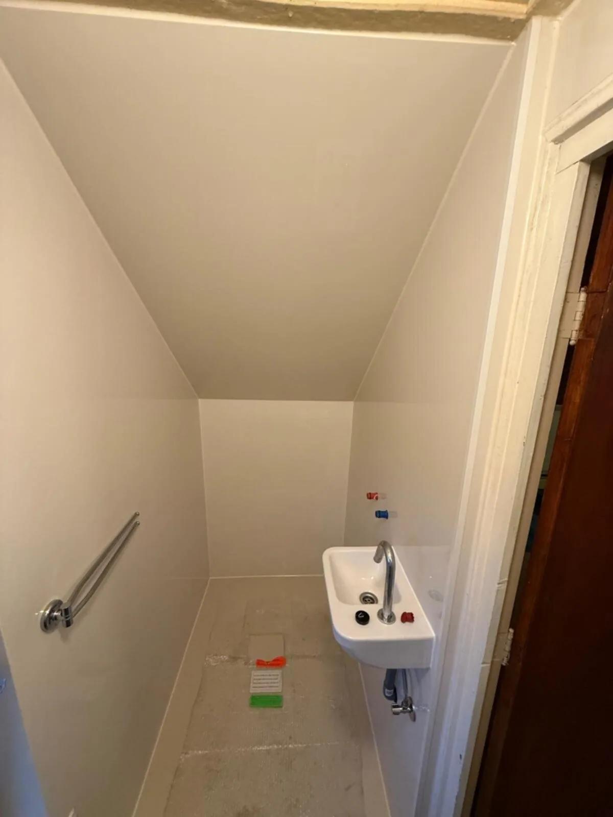 Smalle wc onder de trap met nieuwe witte wanden, fonteintje en beugel, toilet nog niet geplaatst