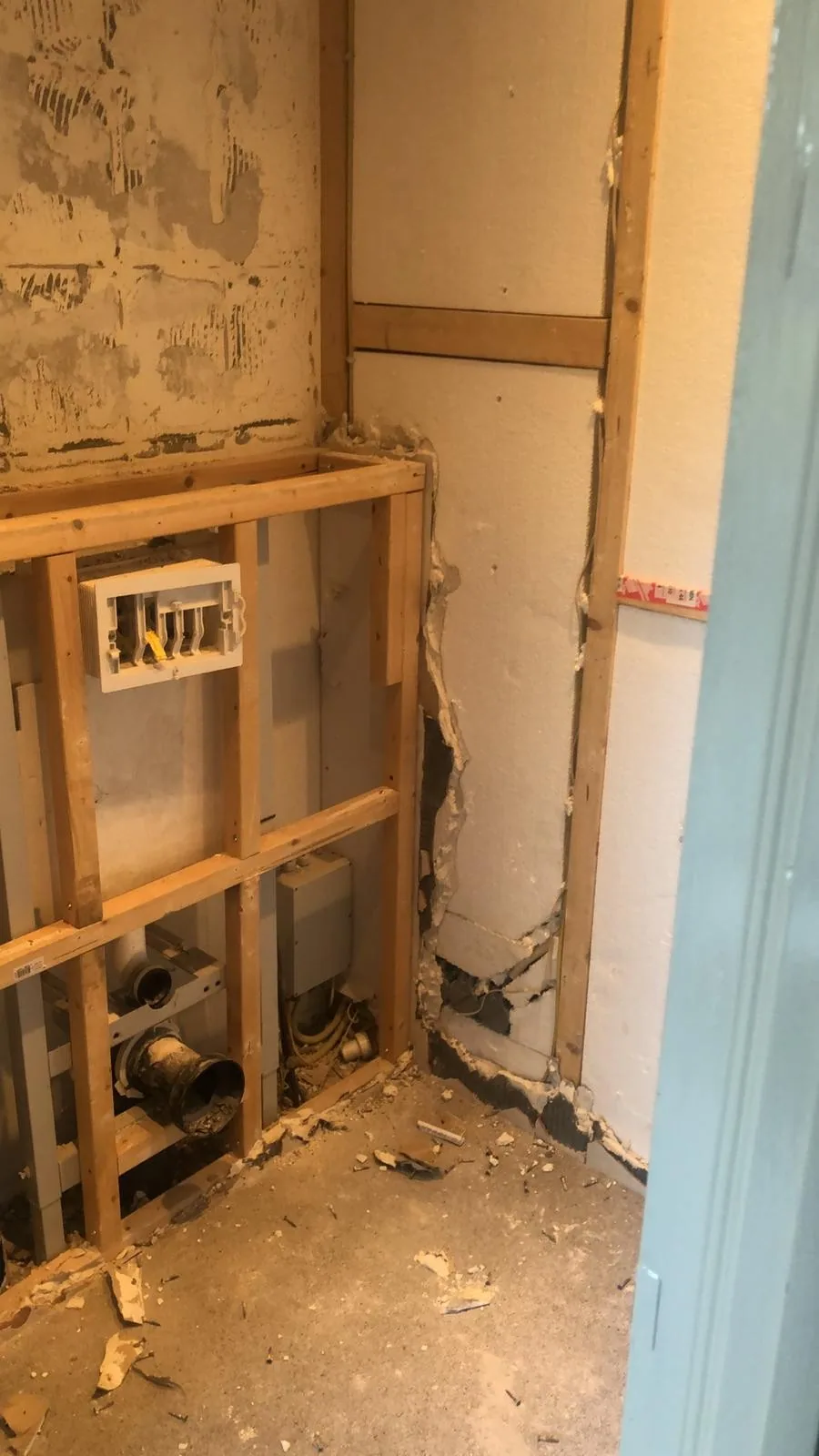Wc na het slopen: houten regelwerk met inbouwreservoir en afvoer zichtbaar, oude wand nog deels aanwezig
